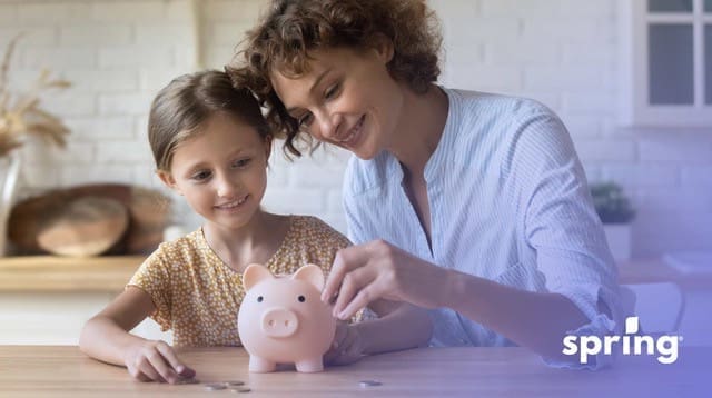 Mother and daughter putting savings in piggy bank